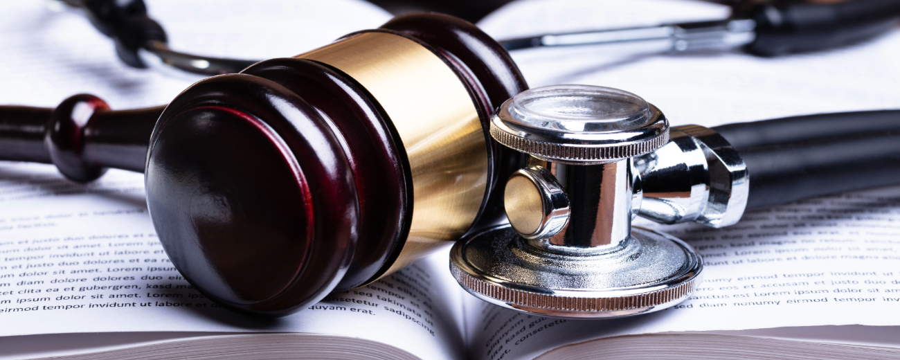 A wooden gavel and a metal stethoscope lying side by side on an open book with visible text on the pages.
